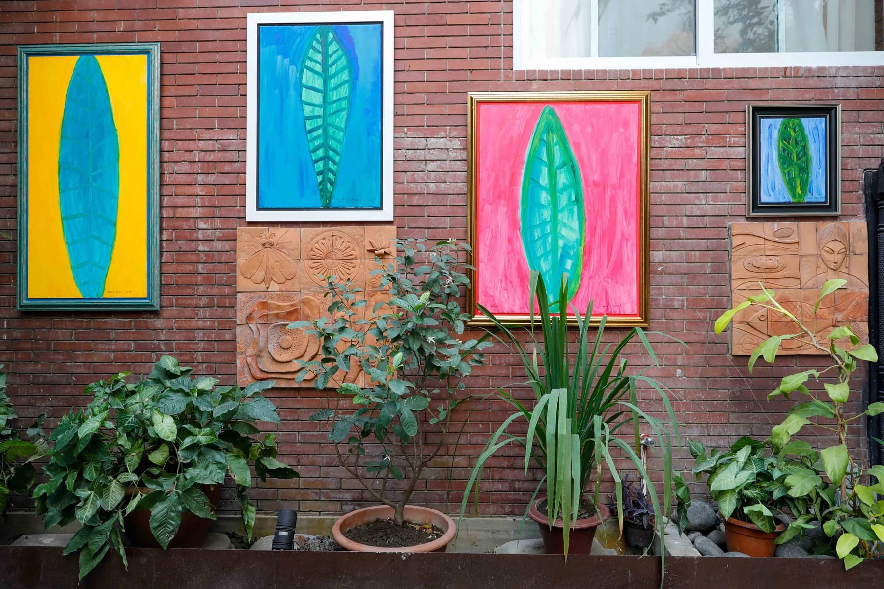 Brightly coloured paintings by Jamil Khan hung on the brick garden wall among plants