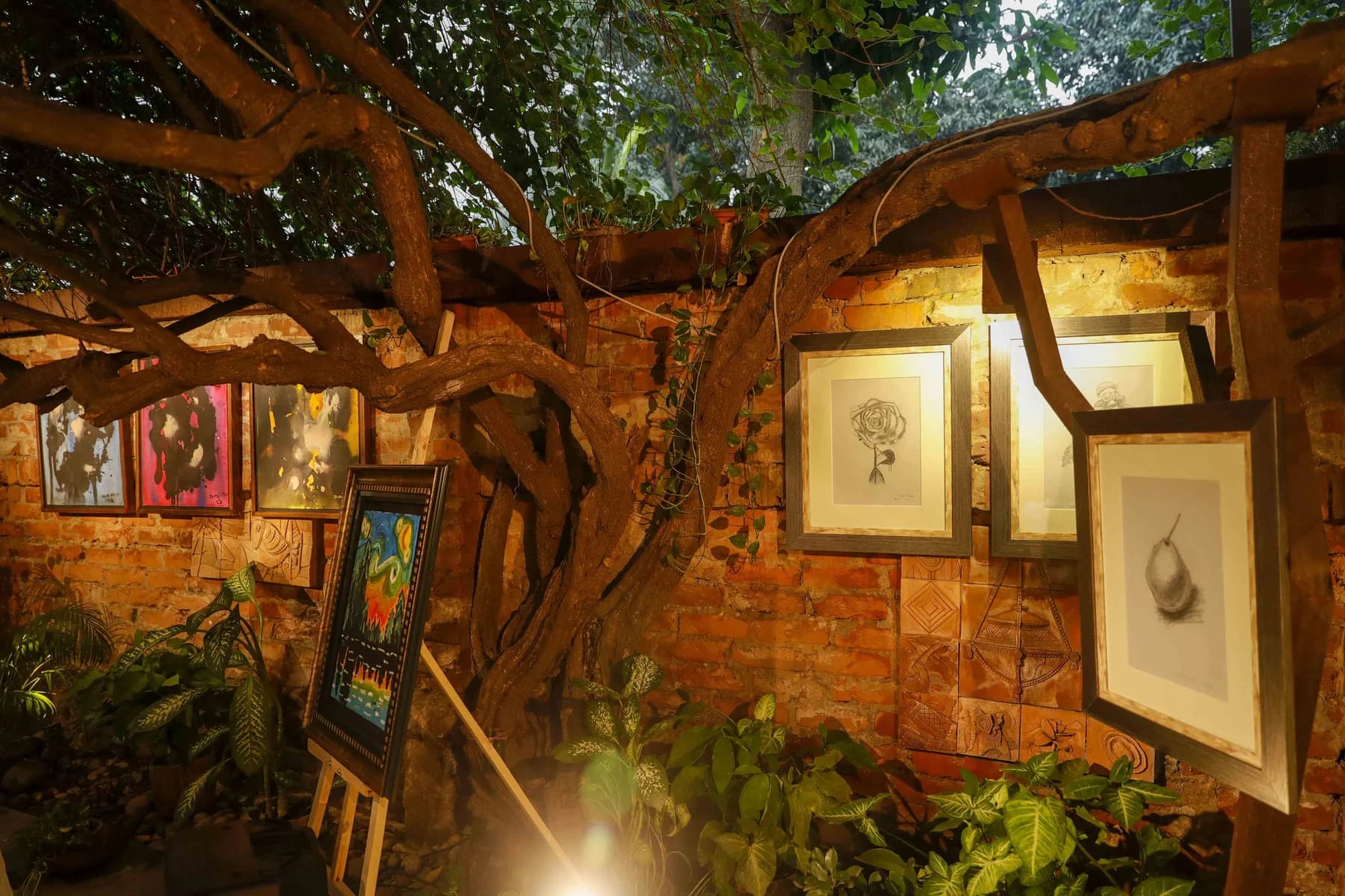 Framed works hung on the brick garden wall beneath the trees