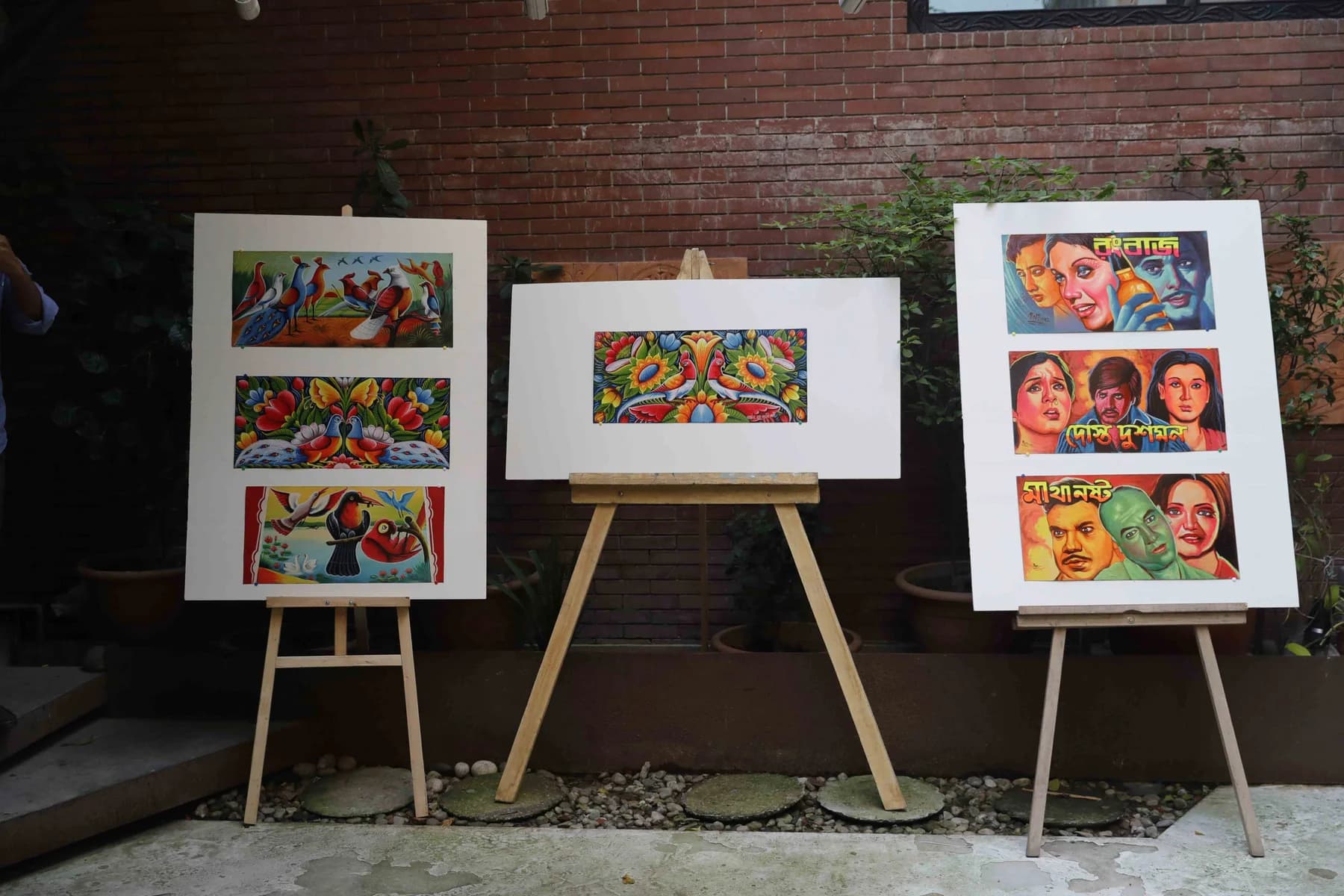 Rickshaw-painted panels shown on easels against the brick garden wall